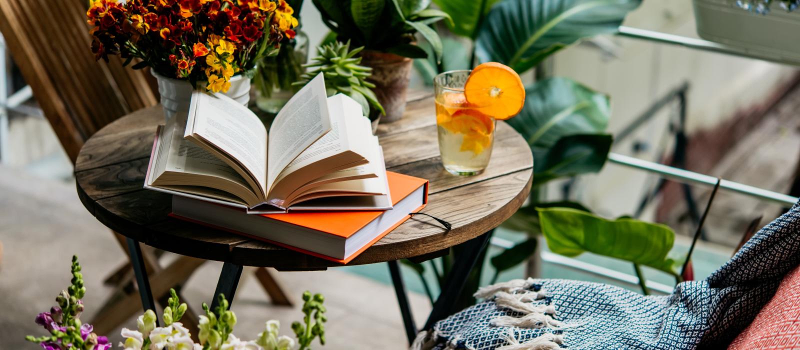 Open book sits on patio table, alongside drink and plants